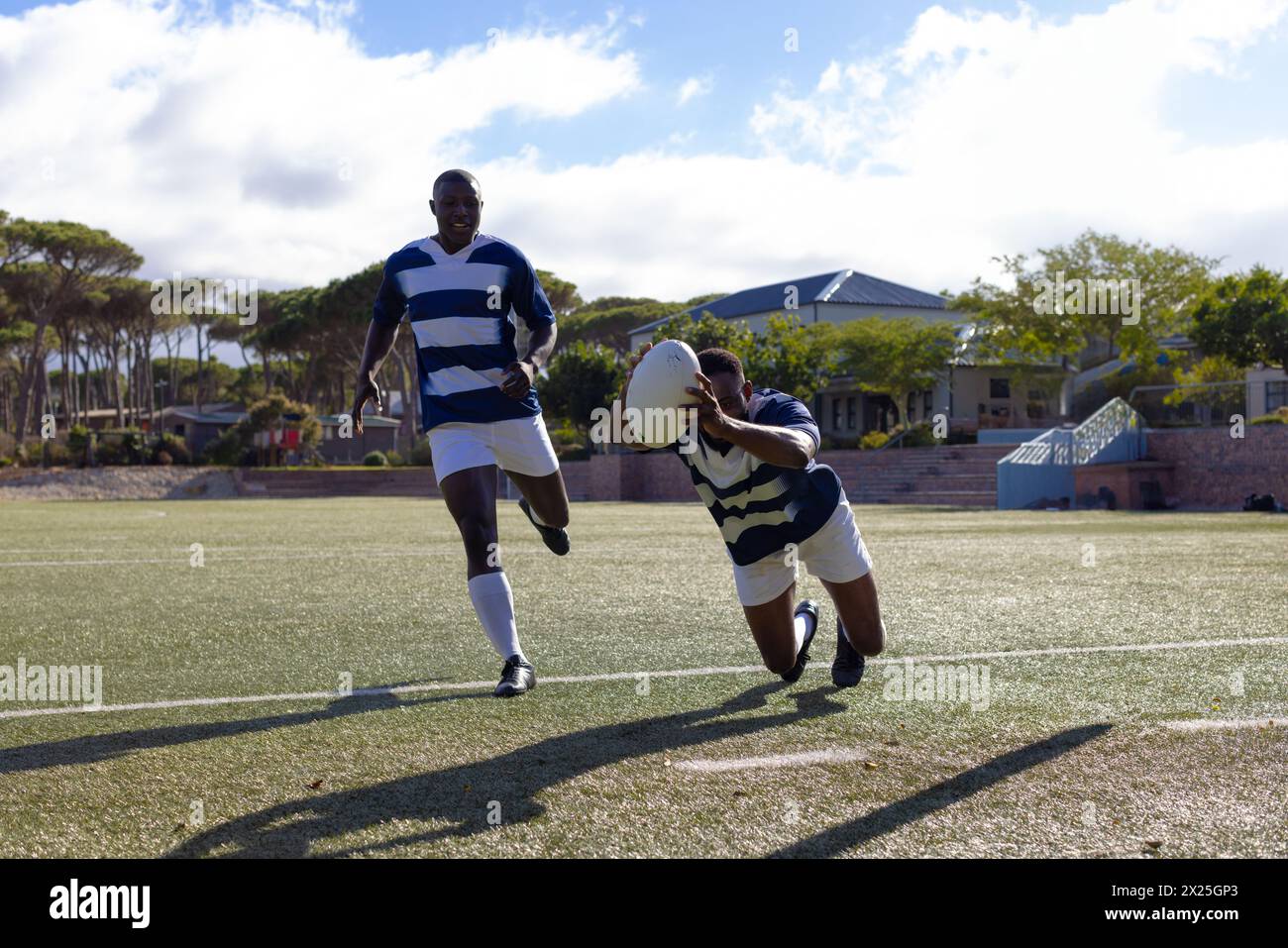 Due giovani atleti afroamericani in maglie a righe giocano a rugby sotto il sole su un campo Foto Stock