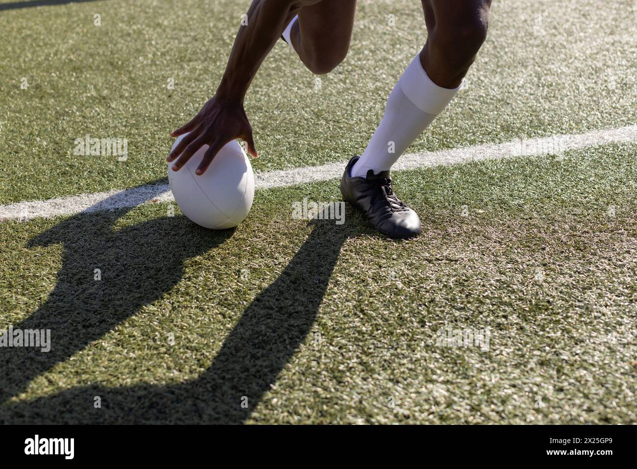 Un giovane atleta afroamericano che indossa articoli sportivi sta mettendo una palla da rugby sull'erba Foto Stock