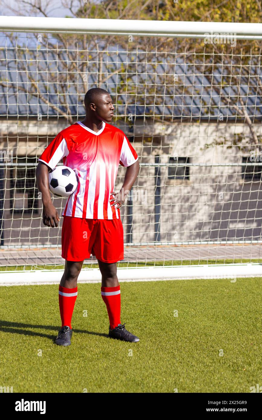 Giovane atleta afroamericano con in mano una palla da calcio, in piedi sul campo all'aperto, copia spazio Foto Stock