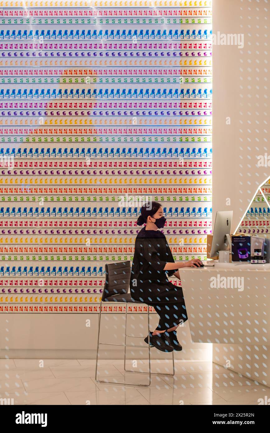 Una donna che indossa una maschera covid seduta al computer in un negozio di Singapore Foto Stock