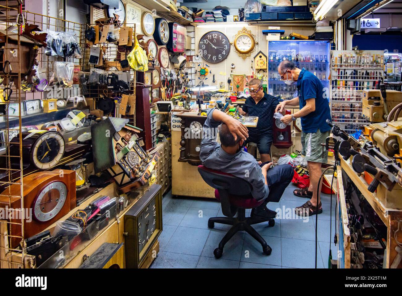 Tre uomini in un negozio di riparazione di orologi e orologi in un mercato a Singapore Foto Stock