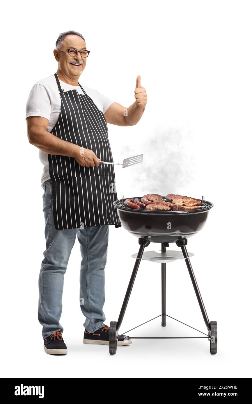 Uomo maturo che grigia la carne su un barbecue e che gesti i pollice isolato su sfondo bianco Foto Stock