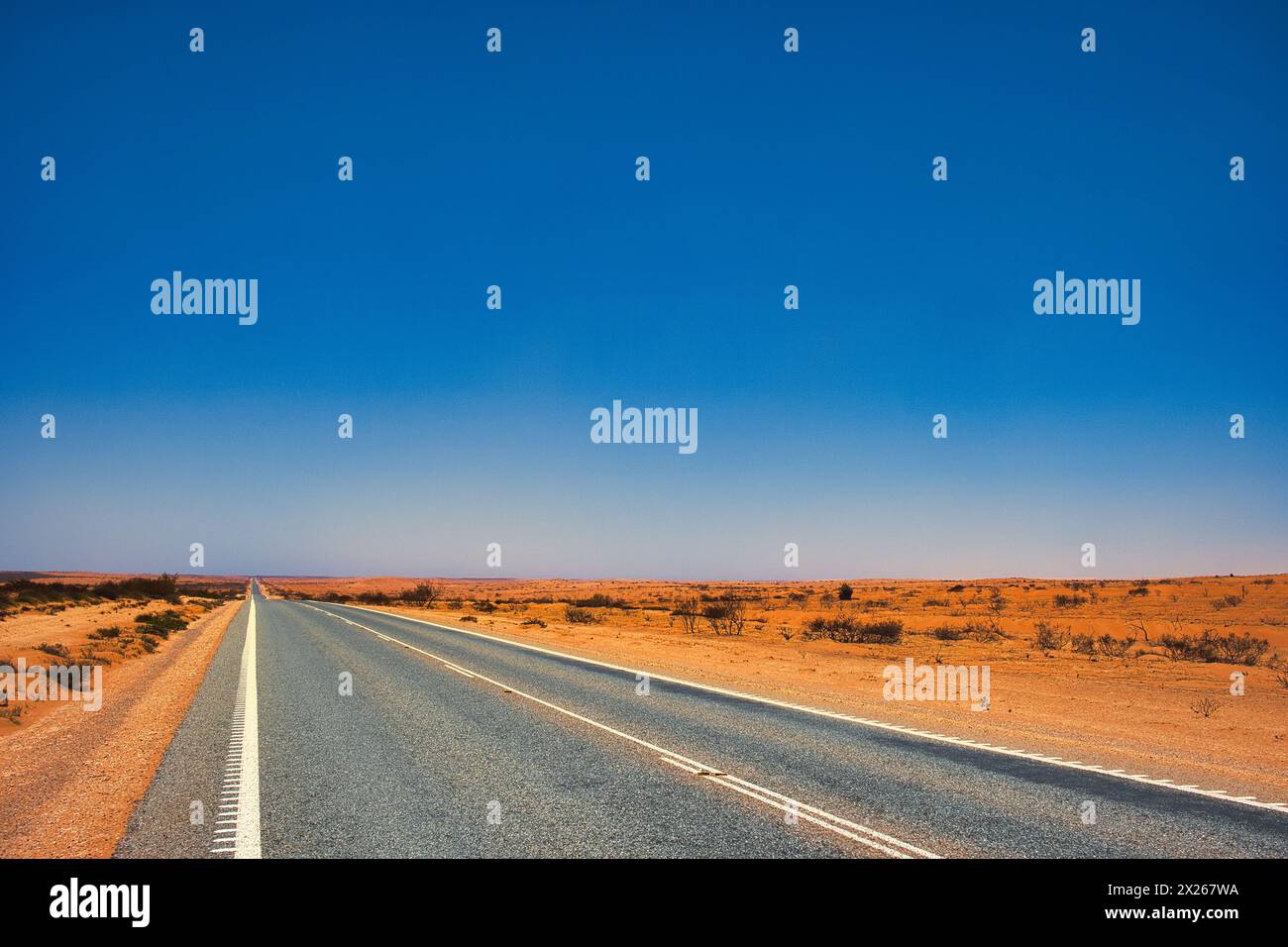Autostrada dritta attraverso un paesaggio desolato di polvere e terra rossa nell'entroterra dell'Australia Occidentale, tra Exmouth e Coral Bay. Foto Stock