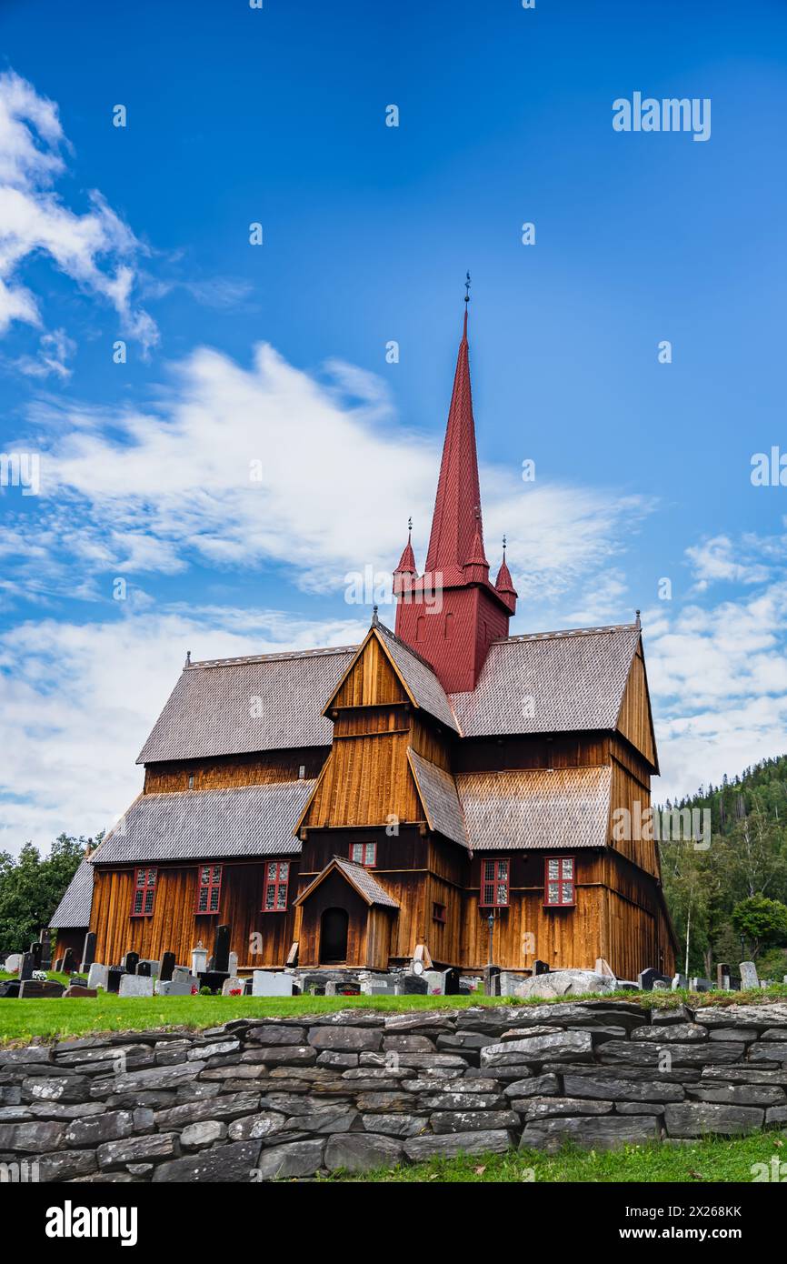 La chiesa medievale del XIII secolo Ringebu Stave si erge tra lapidi sotto un cielo blu con nuvole in estate, riecheggiando secoli di eredità norvegese. Foto Stock