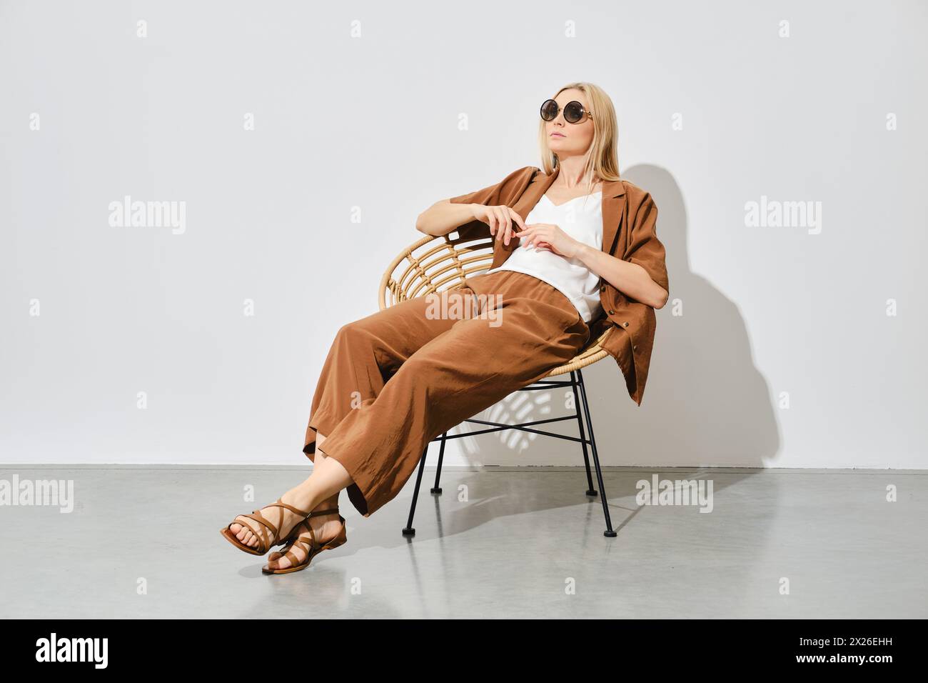 Una donna con un abito morbido si siede rilassata su una sedia in vimini in una stanza luminosa Foto Stock