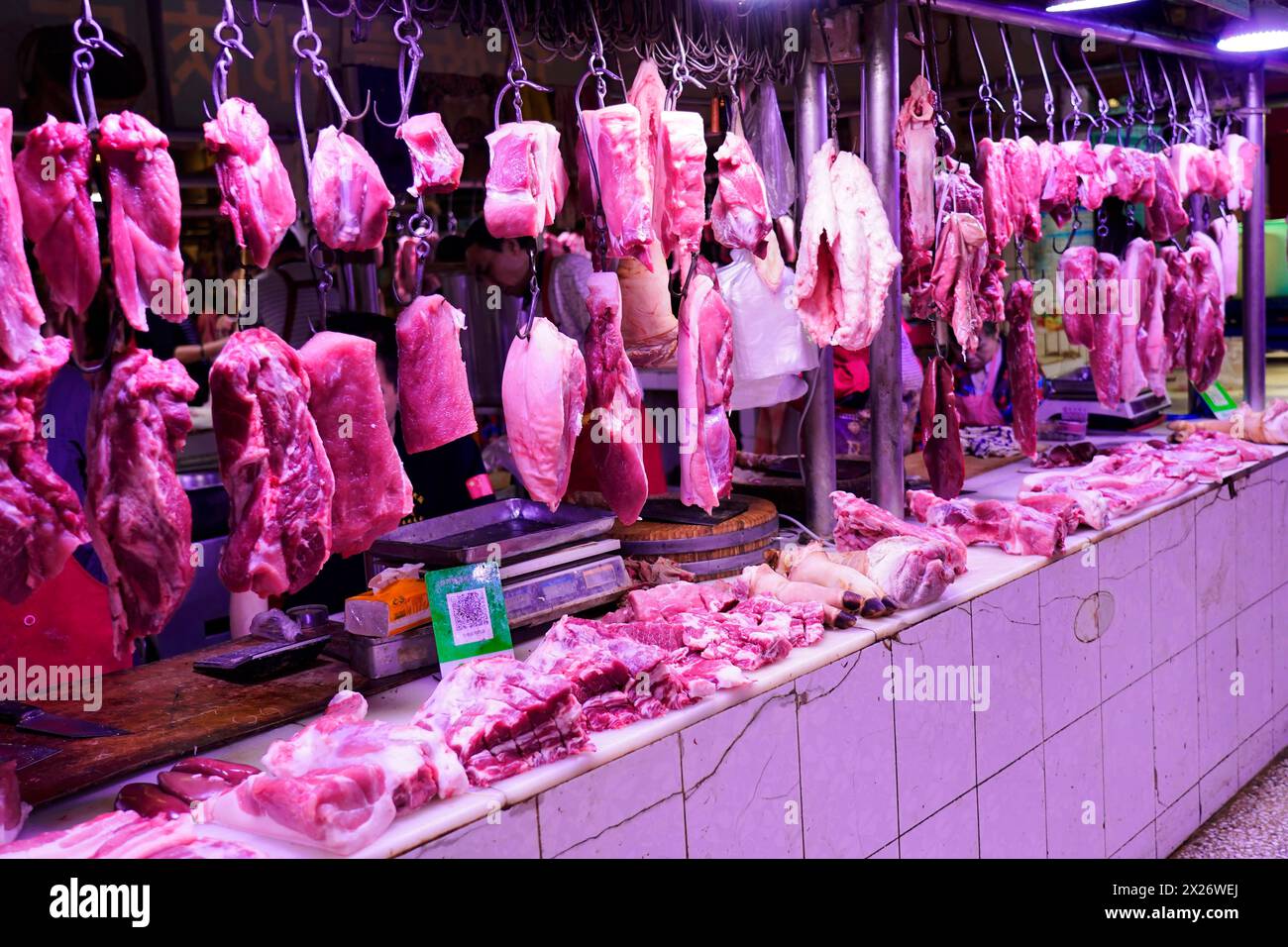 Chongqing, provincia di Chongqing, Cina, pezzi di carne appesi ai ganci in una bancarella di mercato illuminata internamente, Chongqing, provincia di Chongqing, Cina Foto Stock