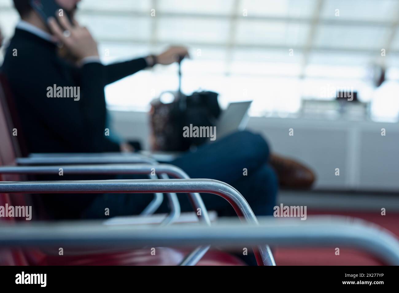 Uomo seduto al cancello d'imbarco dell'aeroporto che parla al telefono e al laptop in grembo mentre aspetta il volo. Parigi, Francia. Messa a fuoco selettiva Foto Stock