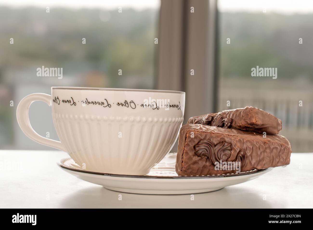 Due fette di torta al cioccolato con piattino bianco in ceramica e tazza sul tavolo vicino alla finestra. Foto Stock