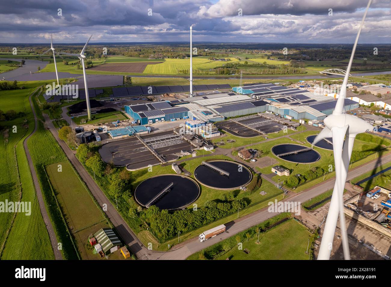 Primo piano di turbine eoliche, trattamento delle acque e impianto di bioenergia. Industria sostenibile nel paesaggio fluviale olandese contro il cielo spettacolare. Antenna circolare Foto Stock