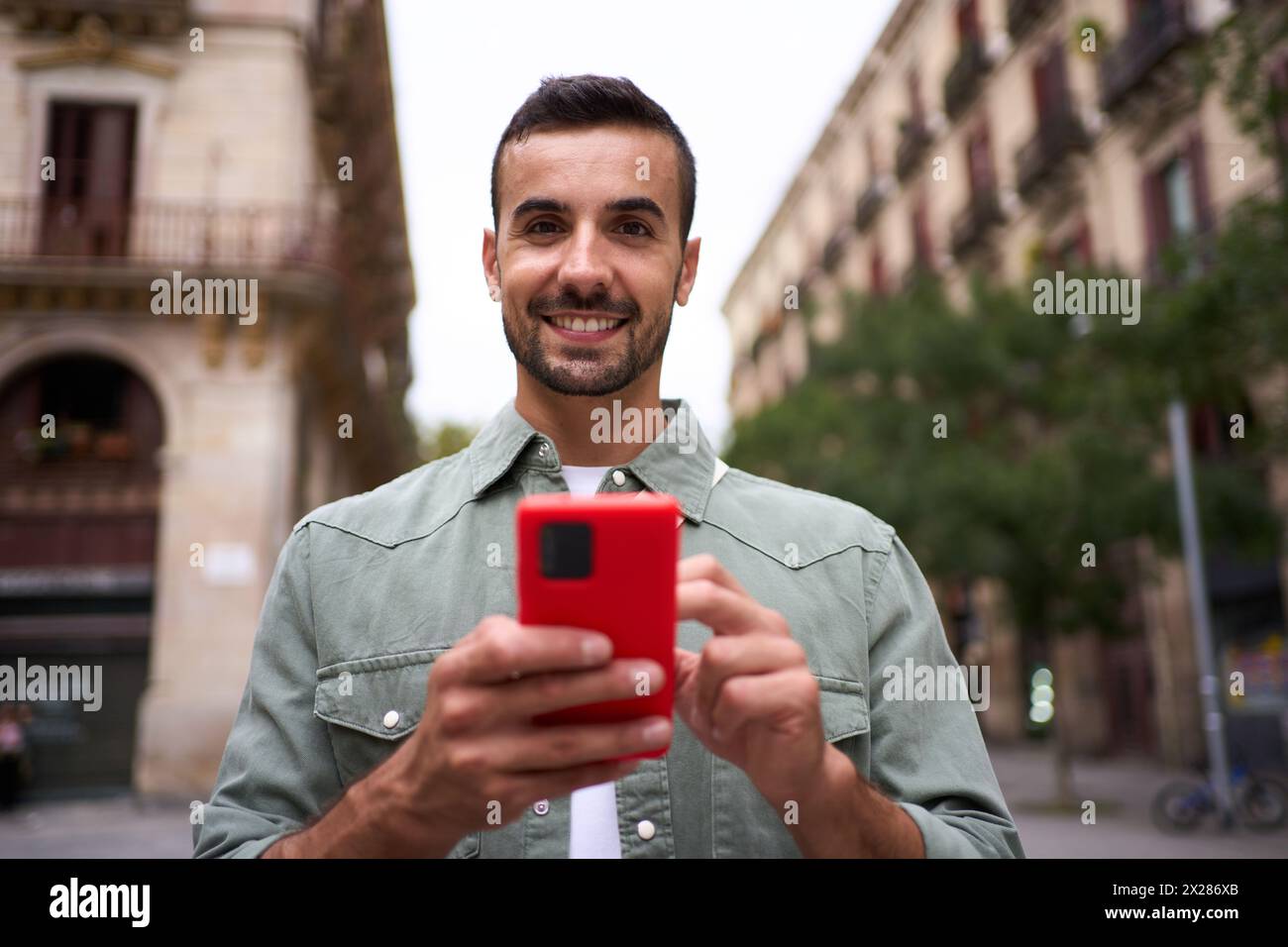 Ritratto il giovane europeo sta sorridendo davanti alla fotocamera che tiene il cellulare nella città di Madrid. Foto Stock