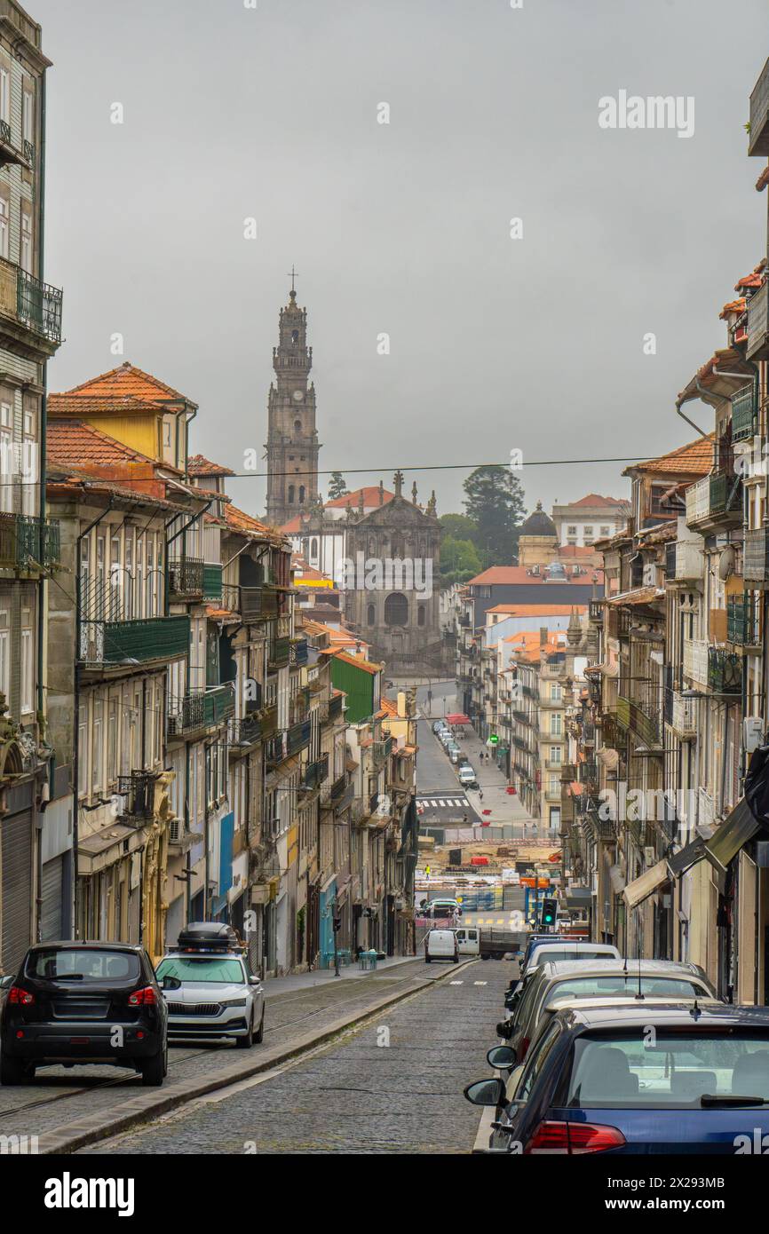 Strada turistica acciottolata a Porto all'alba, con il cielo nuvoloso e la chiesa e la torre dei Clérigos all'estremità avvolta da una nebbia fine. Portogallo. Foto Stock