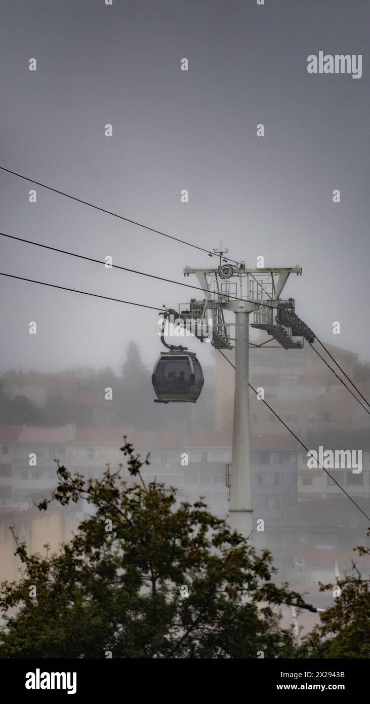 Una funivia Vilanova de Gaia sospesa su cavi d'acciaio sospesi che salgono sotto un cielo nuvoloso con il classico quartiere di Gaia avvolto dalla nebbia Foto Stock