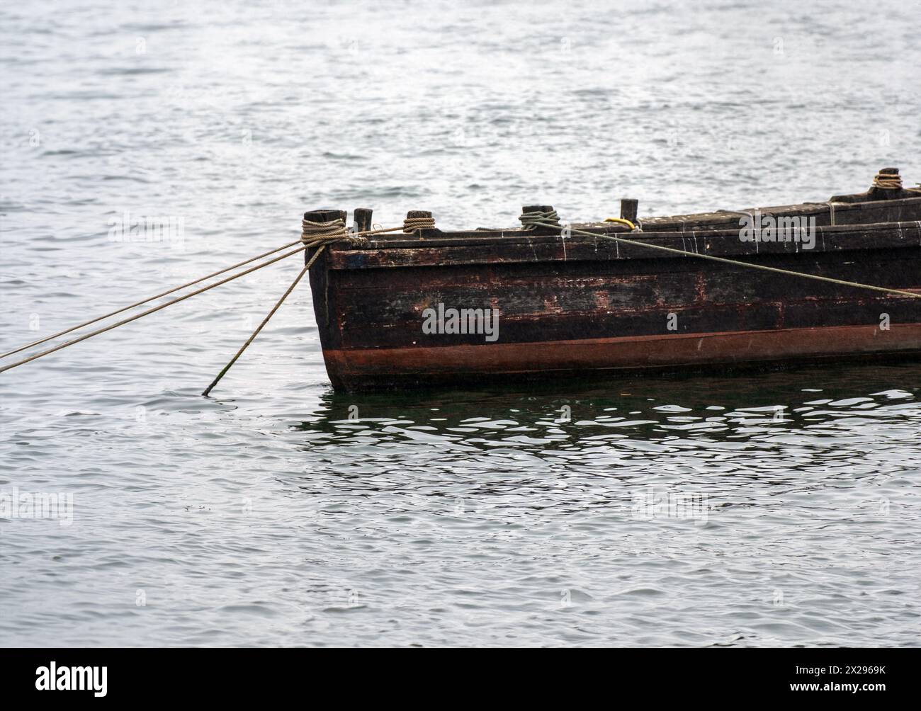 Una piccola vecchia barca in legno, ormeggiata con corde ancorate sul fondo del fiume Douro in una giornata molto nebbiosa. Foto Stock