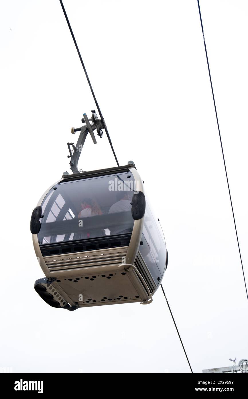 Vista dal basso di una funivia Vila Nova de Gaia con una coppia all'interno sospesa su un cavo d'acciaio sotto un cielo bianco nuvoloso a Porto. Foto Stock