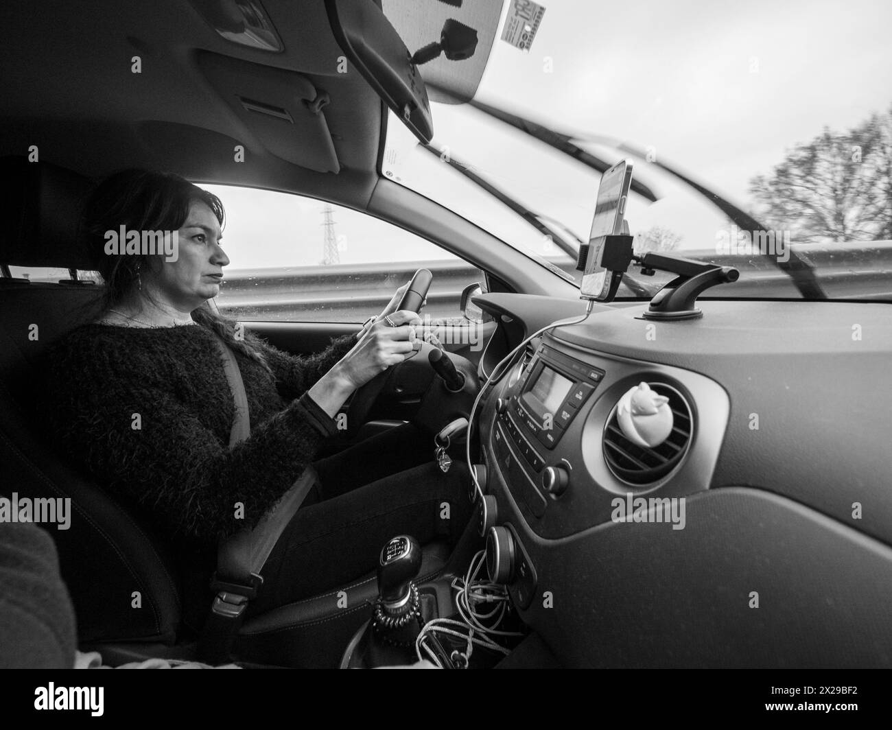 Una donna sta guidando un'auto con un volante e un cruscotto Foto Stock