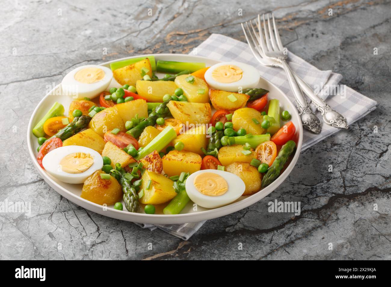 Patate novelle fritte con asparagi, pomodori ciliegini, uova sode e piselli verdi da vicino in un piatto sul tavolo. Orizzontale Foto Stock