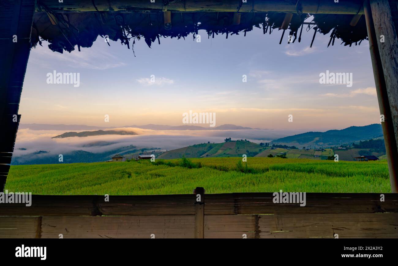 Una vista di un campo con un cielo nebbioso e montagne sullo sfondo. Il cielo è un mix di sfumature blu e arancio che crea un'atmosfera serena e tranquilla Foto Stock