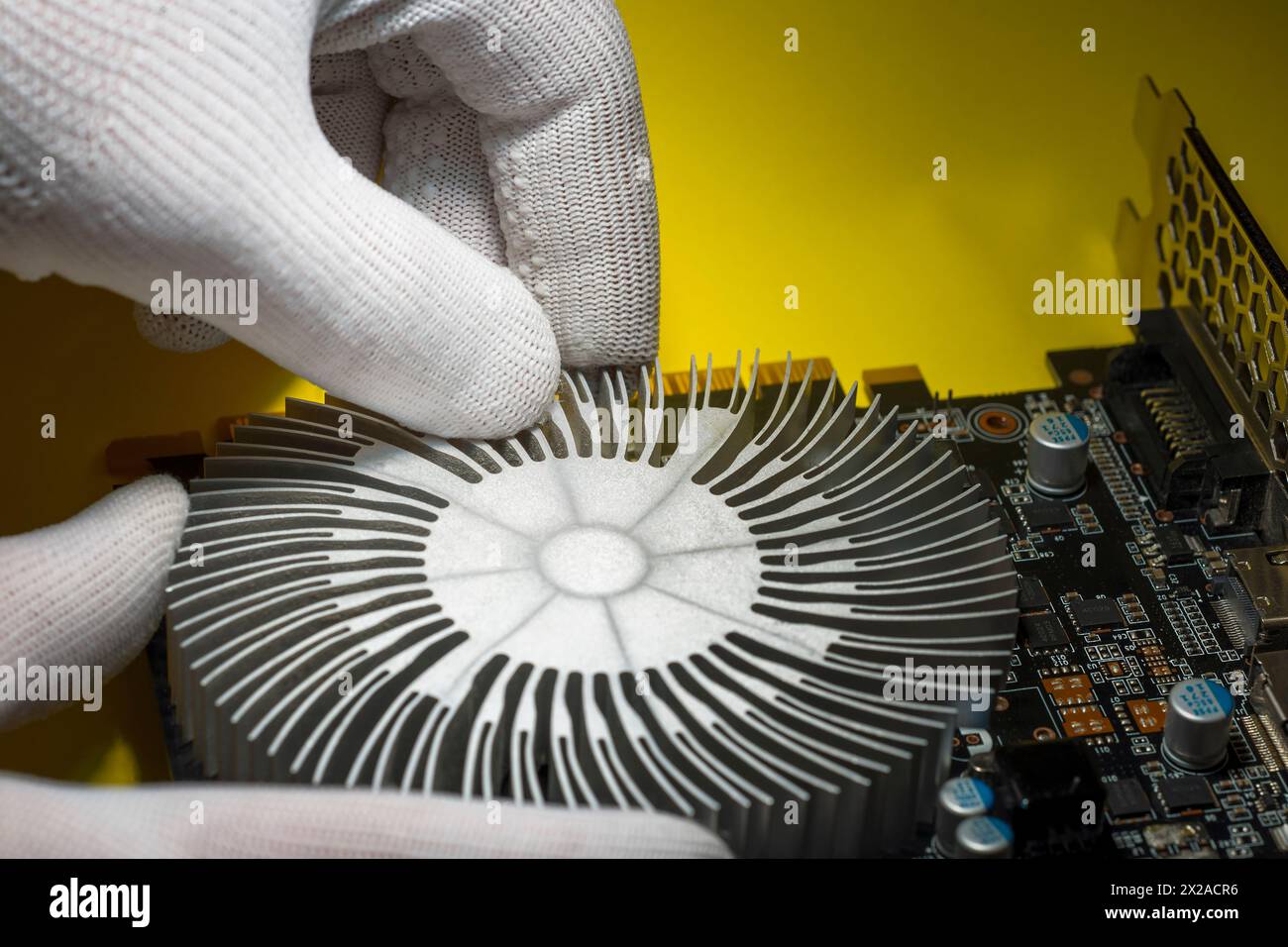Un tecnico con guanti antistatici bianchi che assembla il radiatore di raffreddamento sulla scheda grafica del computer Foto Stock