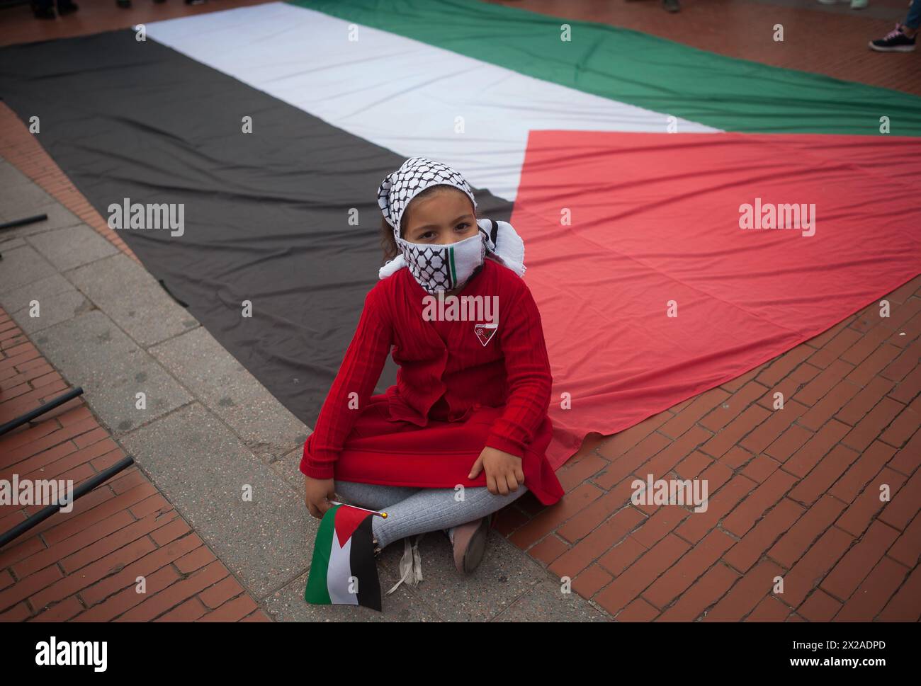 Malaga, Spagna. 21 aprile 2024. Una ragazza coperta da un kufiya siede su una grande bandiera palestinese in piazza Plaza de la Marina prima di prendere parte a una manifestazione nazionale in solidarietà con il popolo palestinese, a seguito dei conflitti tra Israele e Hamas. Con lo slogan "fermare il genocidio in Palestina”, centinaia di persone chiedono la fine del commercio di armi e delle relazioni commerciali con Israele. Credito: SOPA Images Limited/Alamy Live News Foto Stock