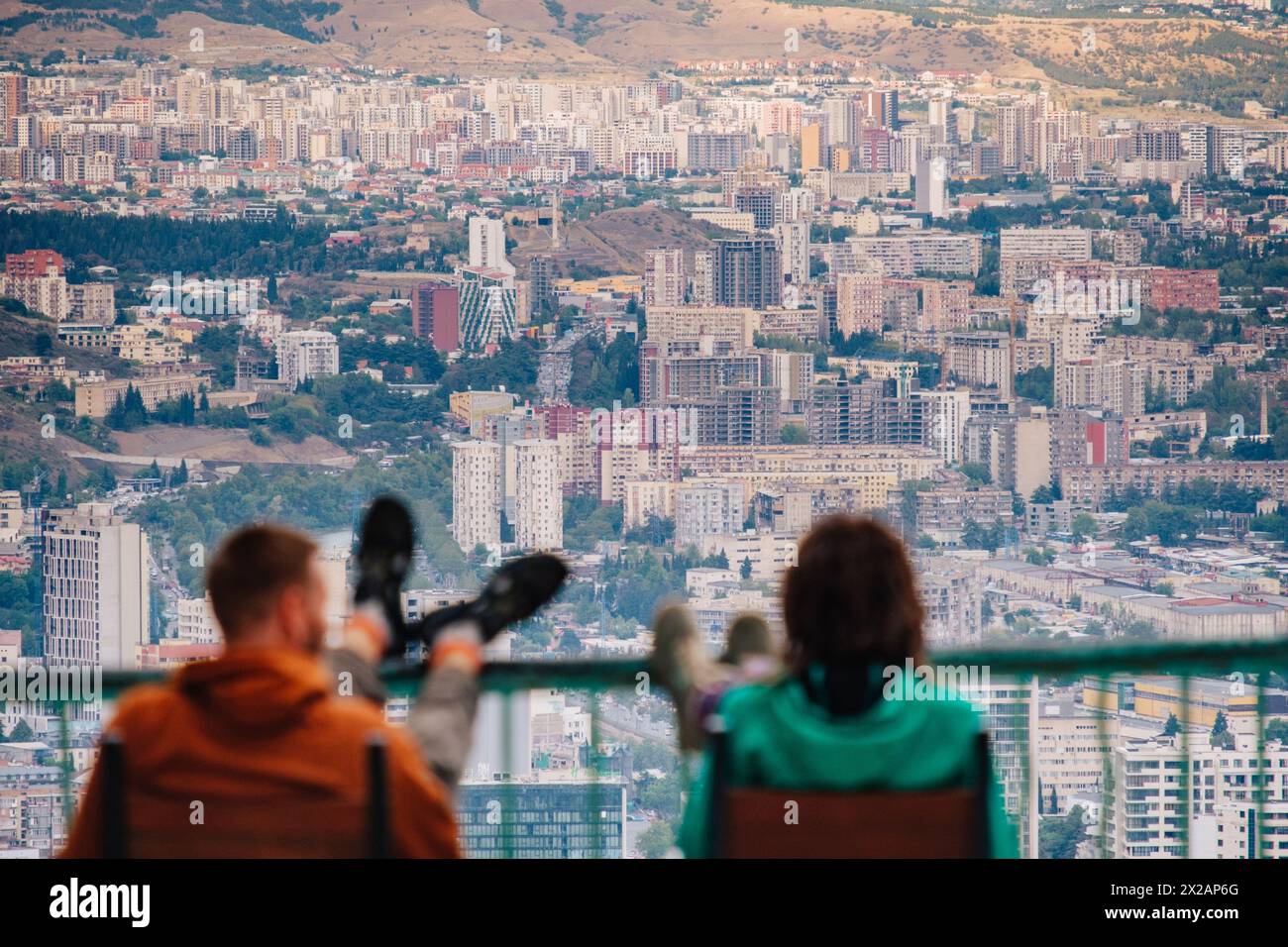 Due persone sedute al parco Mtatsminda, sopra gli edifici dell'era sovietica di Tbilisi, Georgia Foto Stock