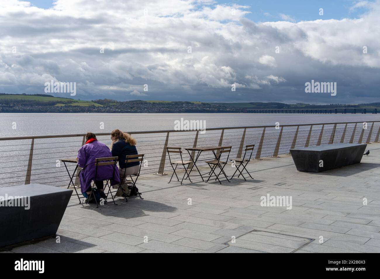 Due persone siedono a un tavolo all'aperto con vista sull'estuario del fiume Tay a Dundee, Scozia, Regno Unito. Concetto di stile di vita urbano moderno, vita urbana Foto Stock
