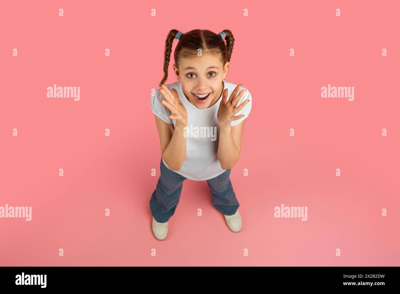 Giovane ragazza felice con trecce sorridenti su sfondo rosa Foto Stock