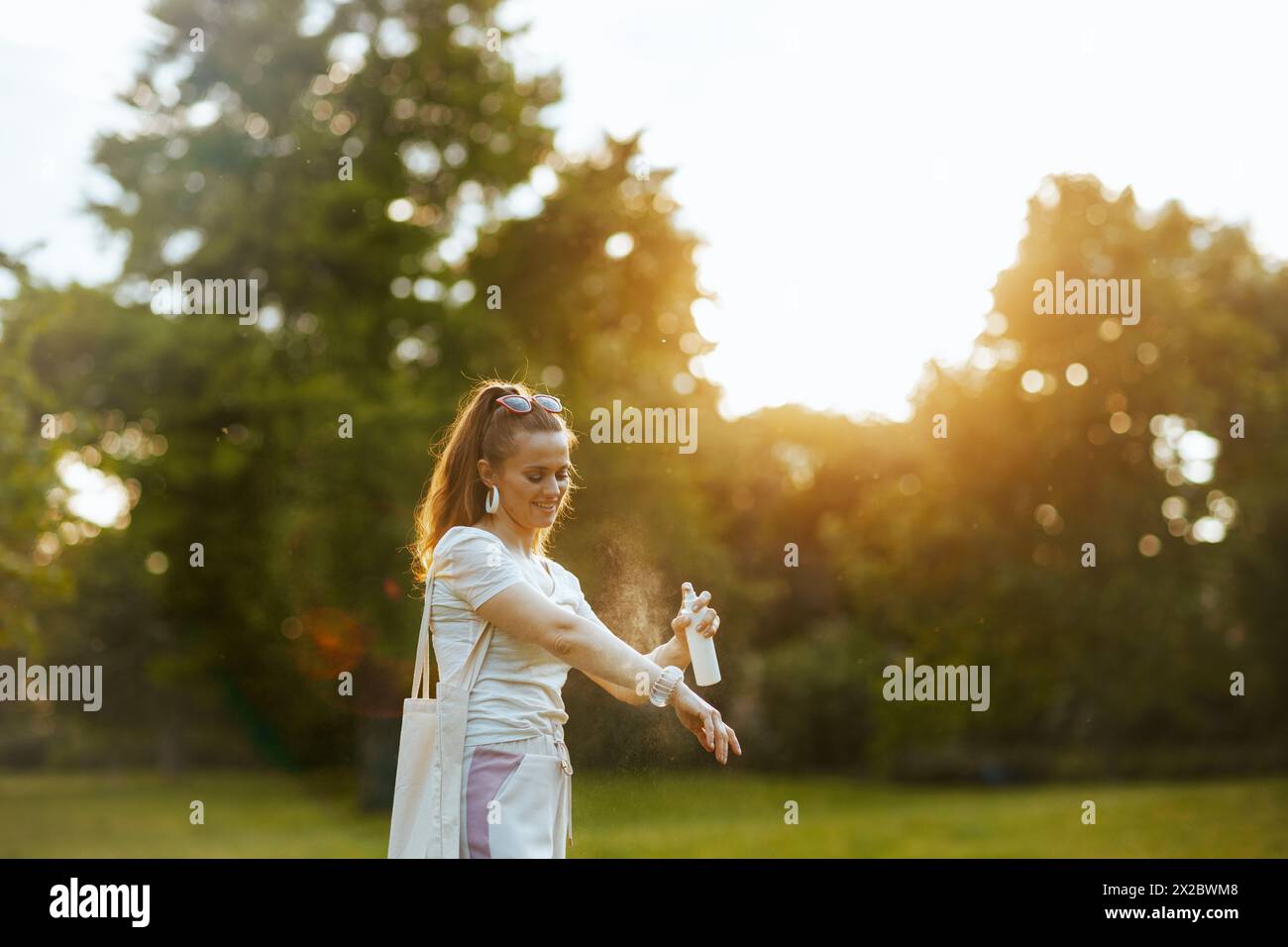 Ora legale. felice donna moderna di 40 anni in camicia bianca con borsa tote con acari spruzzati nel prato esterno in natura. Foto Stock