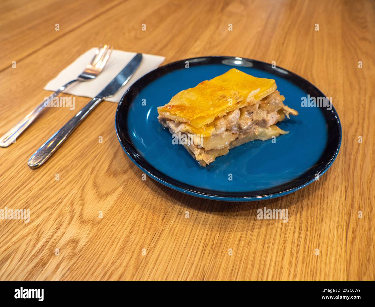 Un pezzo di casseruola di patate con funghi e pollo ricoperto da crosta di formaggio sul piatto blu scuro Foto Stock