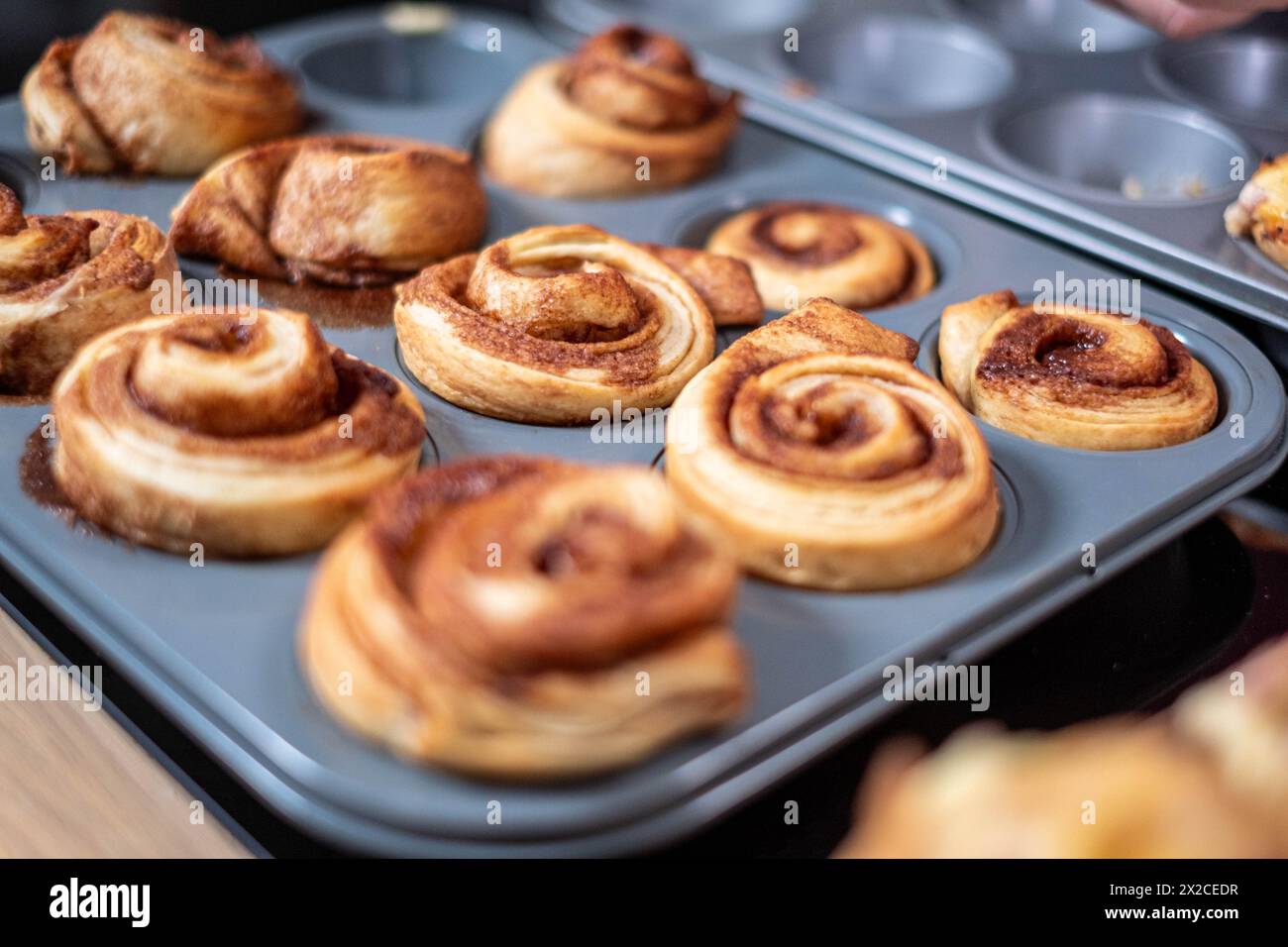 Panini alla cannella appena sfornati raffreddati in una scatola per muffin, con un turbinio dorato alla cannella visibile, ambiente da cucina, deliziosi dessert fatti in casa. Alta qualità Foto Stock