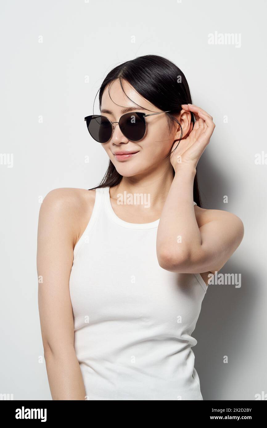 Una donna asiatica che indossa occhiali da sole su sfondo bianco e capovolge i capelli Foto Stock
