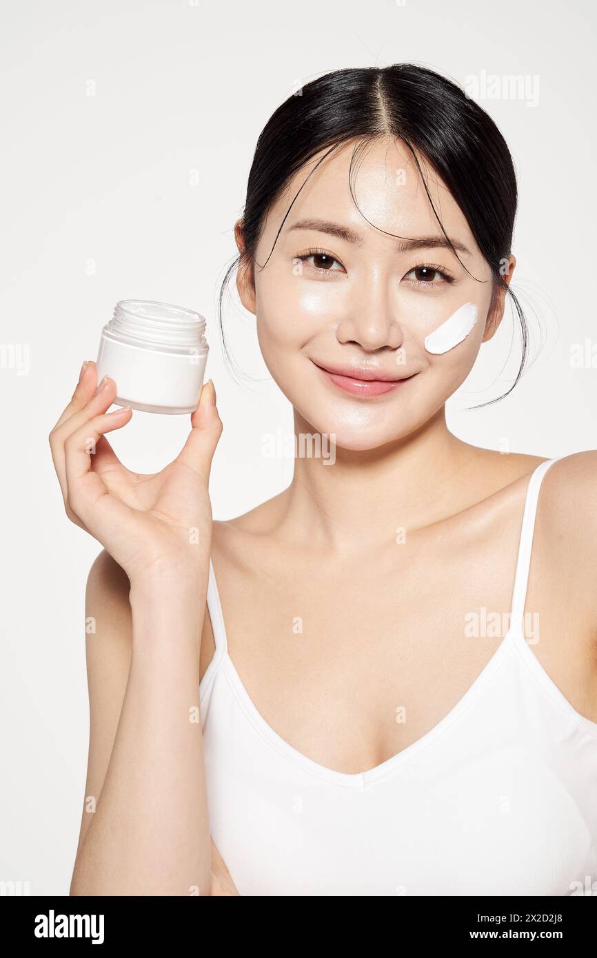 Una donna asiatica con crema sul viso e con cosmetici in mano Foto Stock