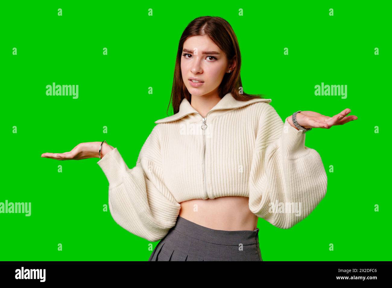 Una giovane donna si trova in uno sfondo verde vibrante, la sua espressione di incertezza o confusione. Foto Stock