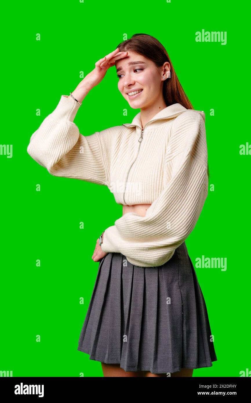 Giovane donna in maglione bianco e gonna grigia sorridente su sfondo verde Foto Stock
