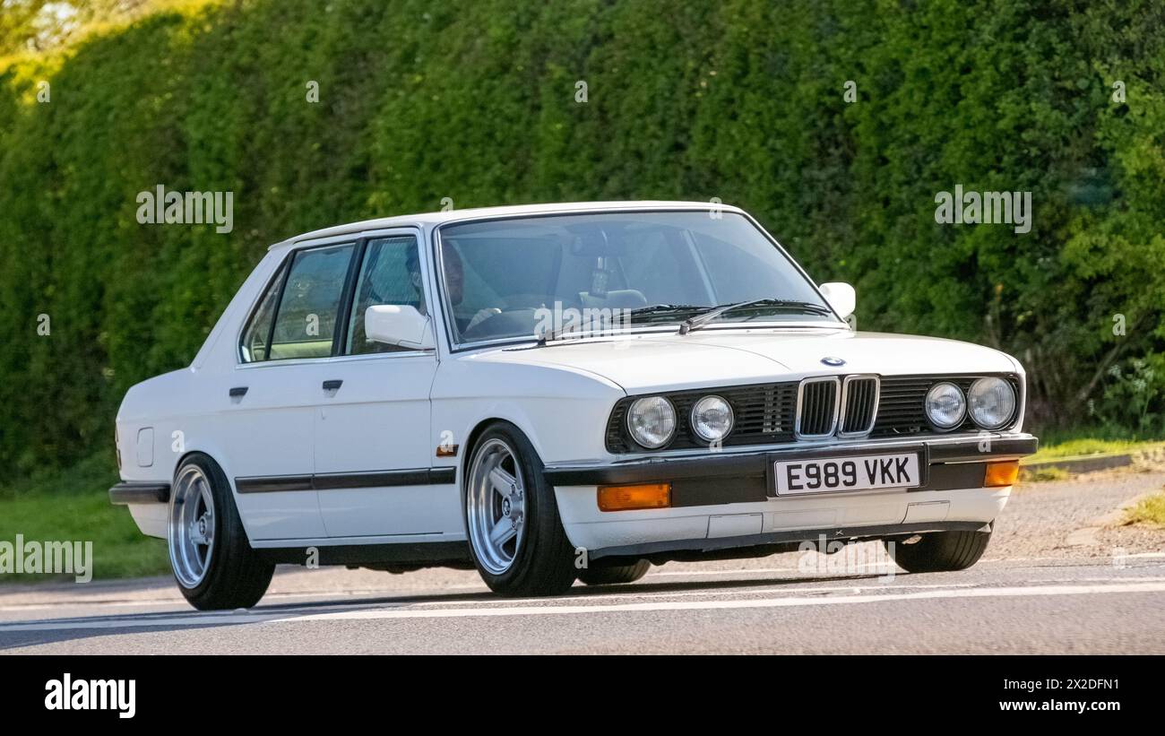 Bicester, Regno Unito - 21 aprile 2024: 1988 BMW 520 i lux bianca che guida su una strada britannica Foto Stock