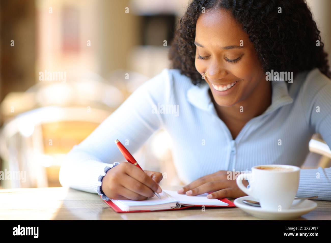 Donna nera felice che scrive all'ordine del giorno seduto in una terrazza del bar Foto Stock