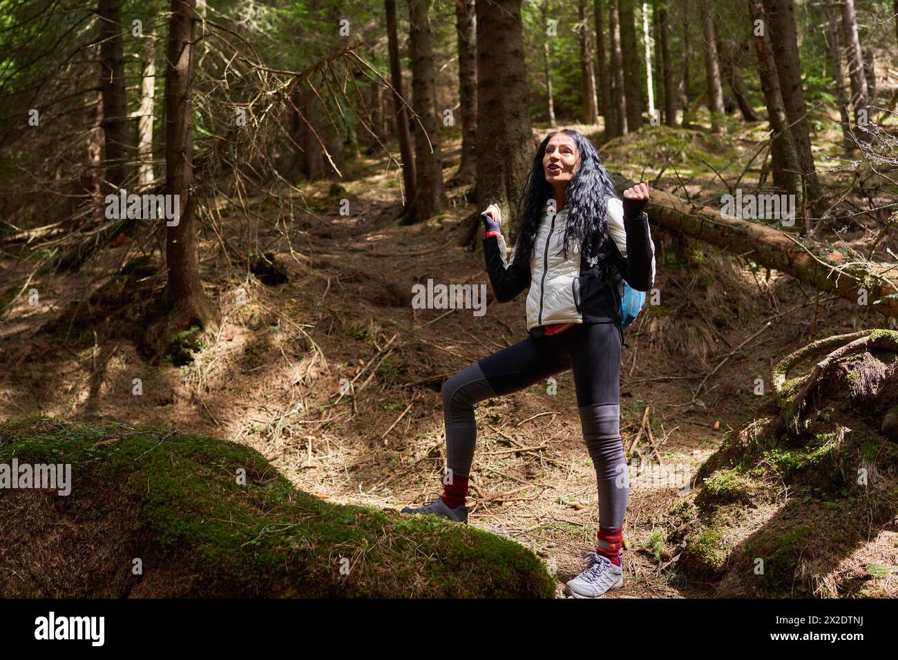Escursionista donna con zaino che cammina su un sentiero tra le montagne con foreste di pini Foto Stock