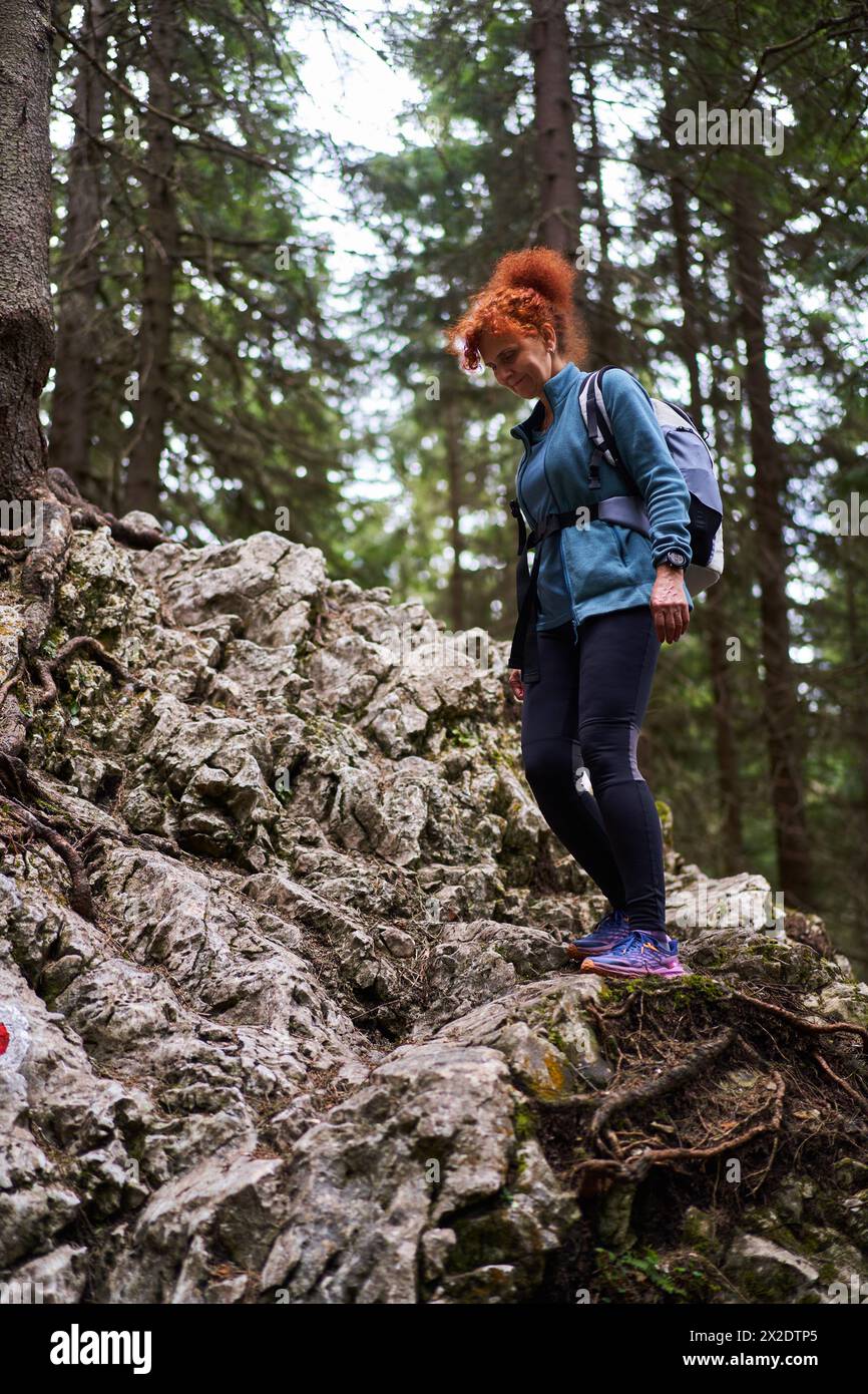 Escursionista donna con zaino che cammina su un sentiero tra le montagne con foreste di pini Foto Stock