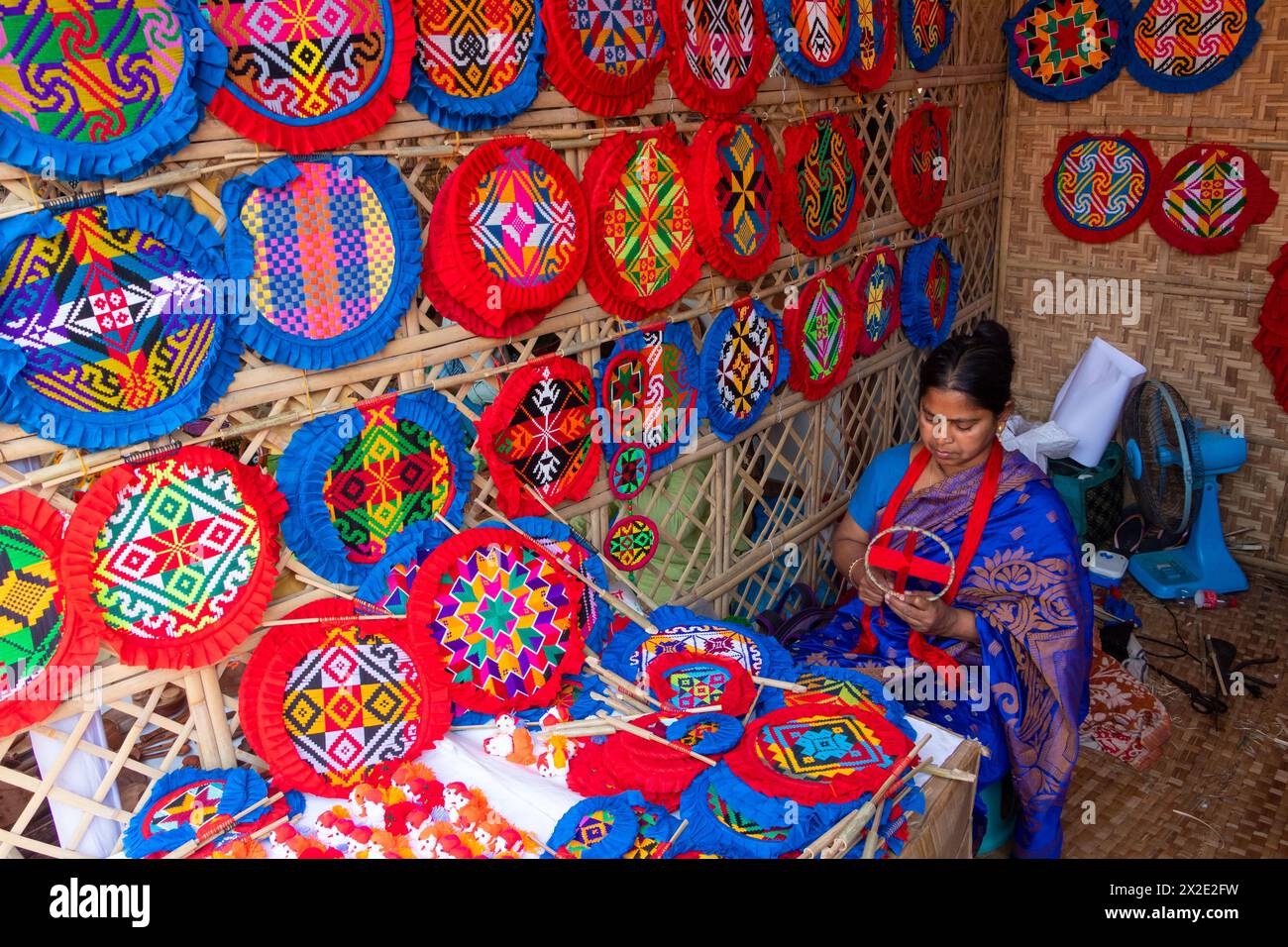 Narayanganj, Dacca, Bangladesh. 22 aprile 2024, Narayanganj, Dacca, Bangladesh: I lavoratori ricamano sapientemente ventilatori a mano con forme geometriche dai colori vivaci a Narayanganj, Bangladesh. Utilizzano bambù e filati colorati per creare ventilatori dal design complesso. Durante le estati calde, danno una brezza fresca che aiuta quando fa davvero caldo all'aperto in caso di distacco del carico. Ogni lavoratore può contare su 10 tifosi al giorno, ogni fan viene venduto per circa 1,20 USD alle fiere dei villaggi. Questa è diventata una professione tradizionale nella zona, fanno fan a mano da centinaia di anni. Credito: ZUMA Press, in Foto Stock