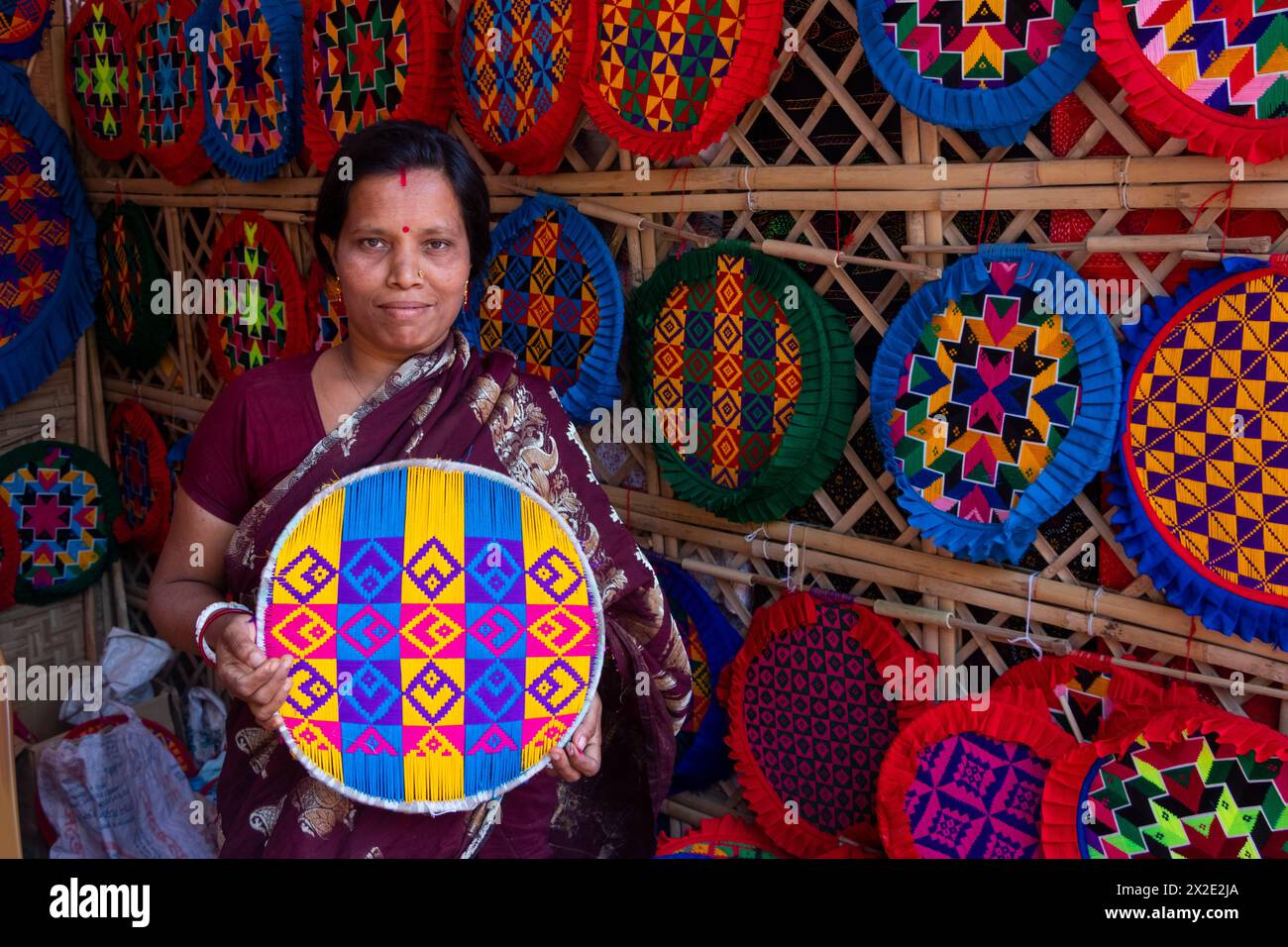 Narayanganj, Dacca, Bangladesh. 22 aprile 2024, Narayanganj, Dacca, Bangladesh: I lavoratori ricamano sapientemente ventilatori a mano con forme geometriche dai colori vivaci a Narayanganj, Bangladesh. Utilizzano bambù e filati colorati per creare ventilatori dal design complesso. Durante le estati calde, danno una brezza fresca che aiuta quando fa davvero caldo all'aperto in caso di distacco del carico. Ogni lavoratore può contare su 10 tifosi al giorno, ogni fan viene venduto per circa 1,20 USD alle fiere dei villaggi. Questa è diventata una professione tradizionale nella zona, fanno fan a mano da centinaia di anni. Credito: ZUMA Press, in Foto Stock