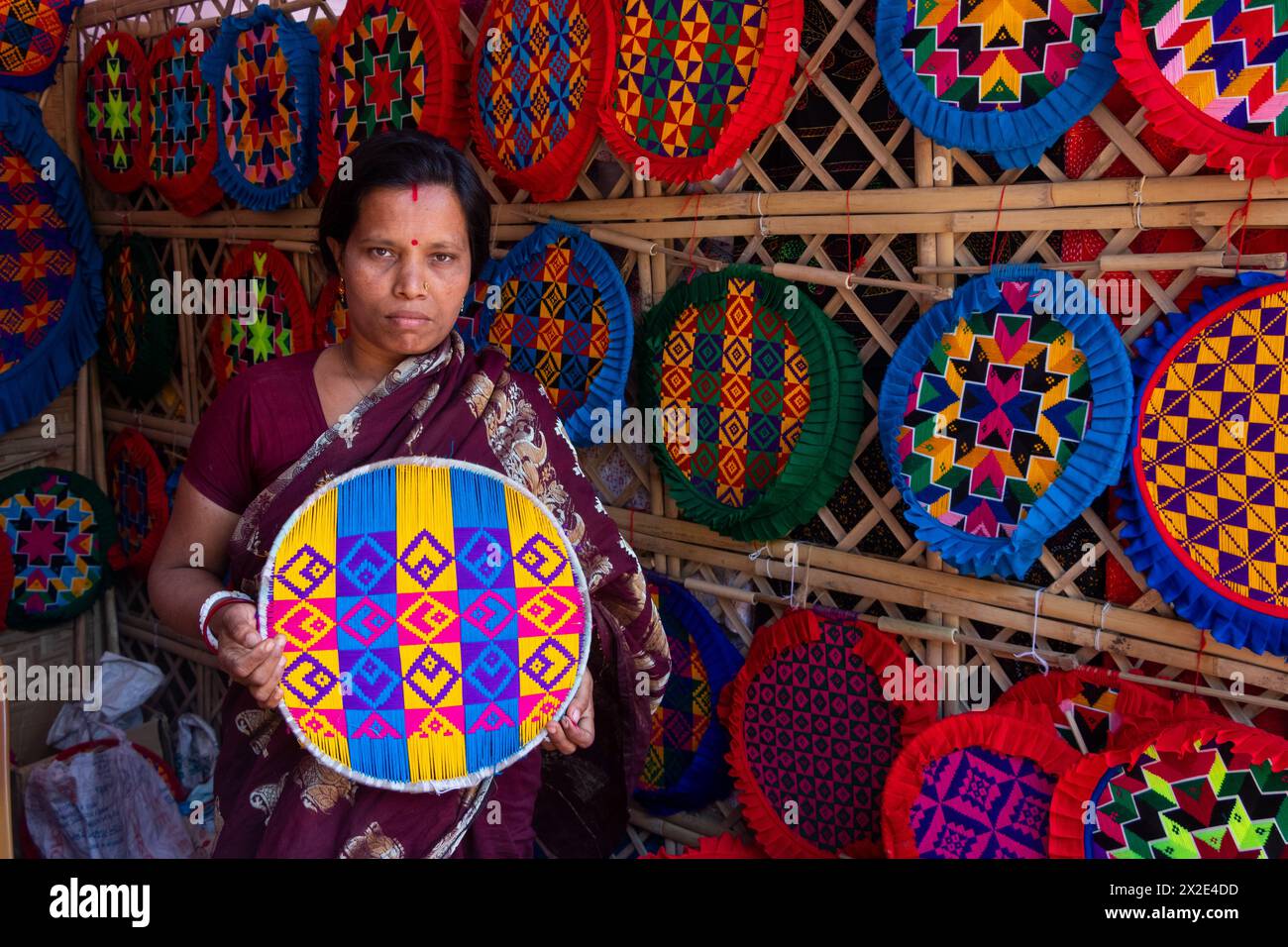 Narayanganj, Dacca, Bangladesh. 22 aprile 2024, Narayanganj, Dacca, Bangladesh: I lavoratori ricamano sapientemente ventilatori a mano con forme geometriche dai colori vivaci a Narayanganj, Bangladesh. Utilizzano bambù e filati colorati per creare ventilatori dal design complesso. Durante le estati calde, danno una brezza fresca che aiuta quando fa davvero caldo all'aperto in caso di distacco del carico. Ogni lavoratore può contare su 10 tifosi al giorno, ogni fan viene venduto per circa 1,20 USD alle fiere dei villaggi. Questa è diventata una professione tradizionale nella zona, fanno fan a mano da centinaia di anni. Credito: ZUMA Press, in Foto Stock