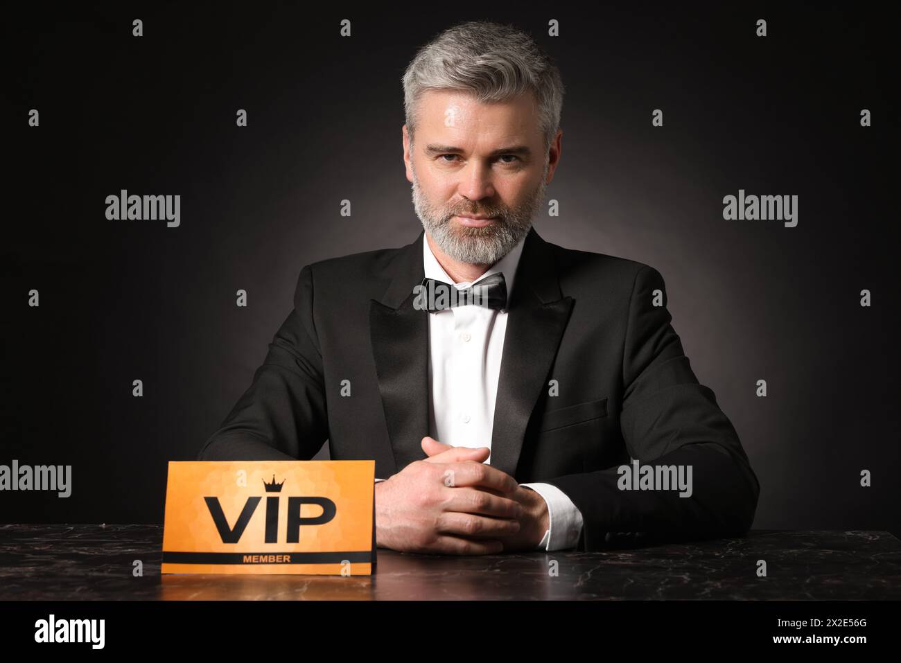 Bell'uomo seduto al tavolo con un cartello VIP su sfondo nero Foto Stock