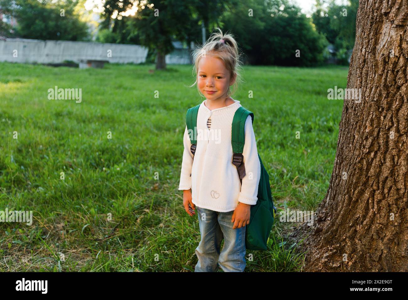 Una giovane ragazza sorridente con uno zaino grande su uno sfondo verde aperto Foto Stock