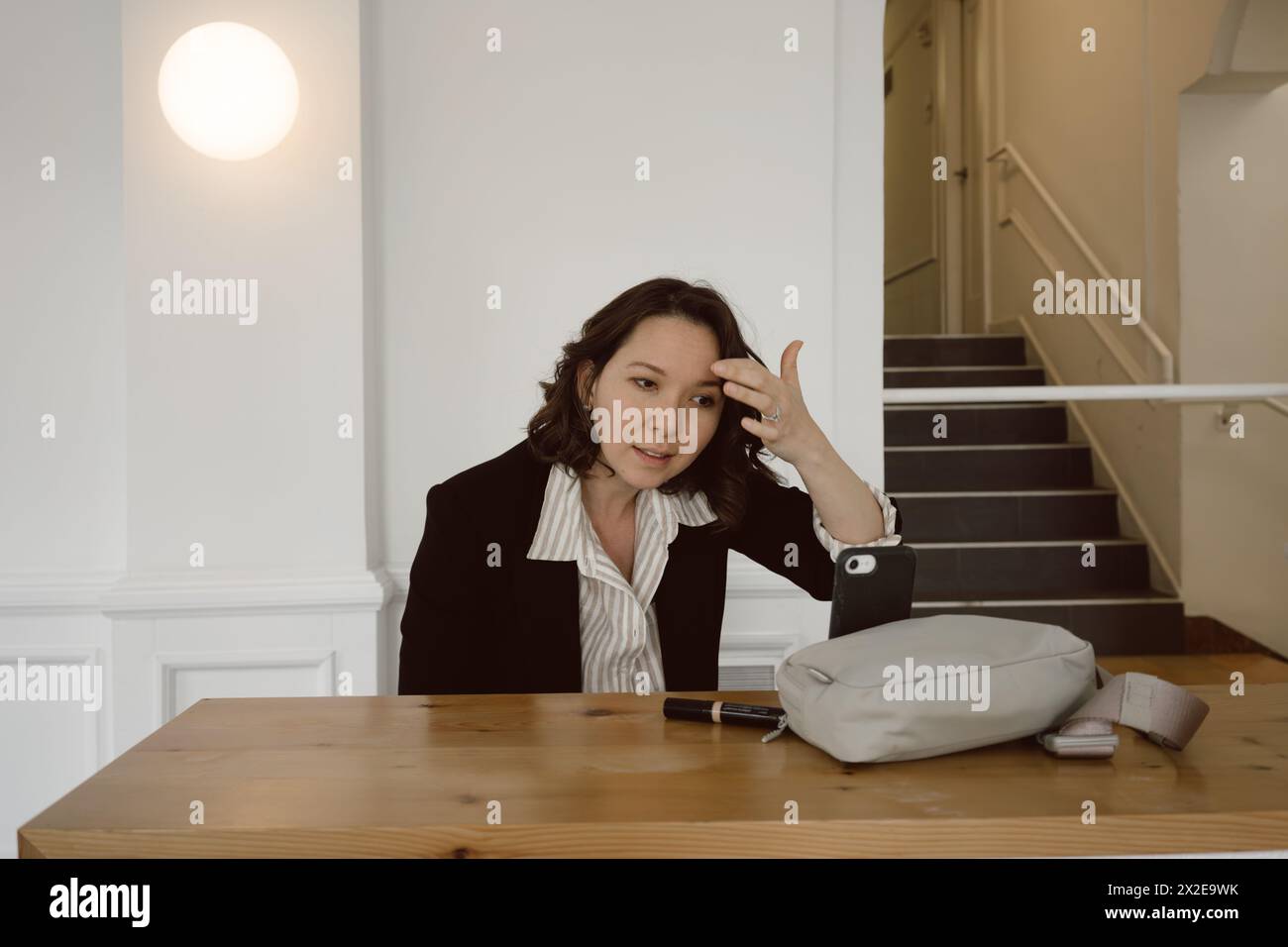 Una donna mezza asiatica tocca il trucco usando il telefono prima di una riunione di lavoro Foto Stock