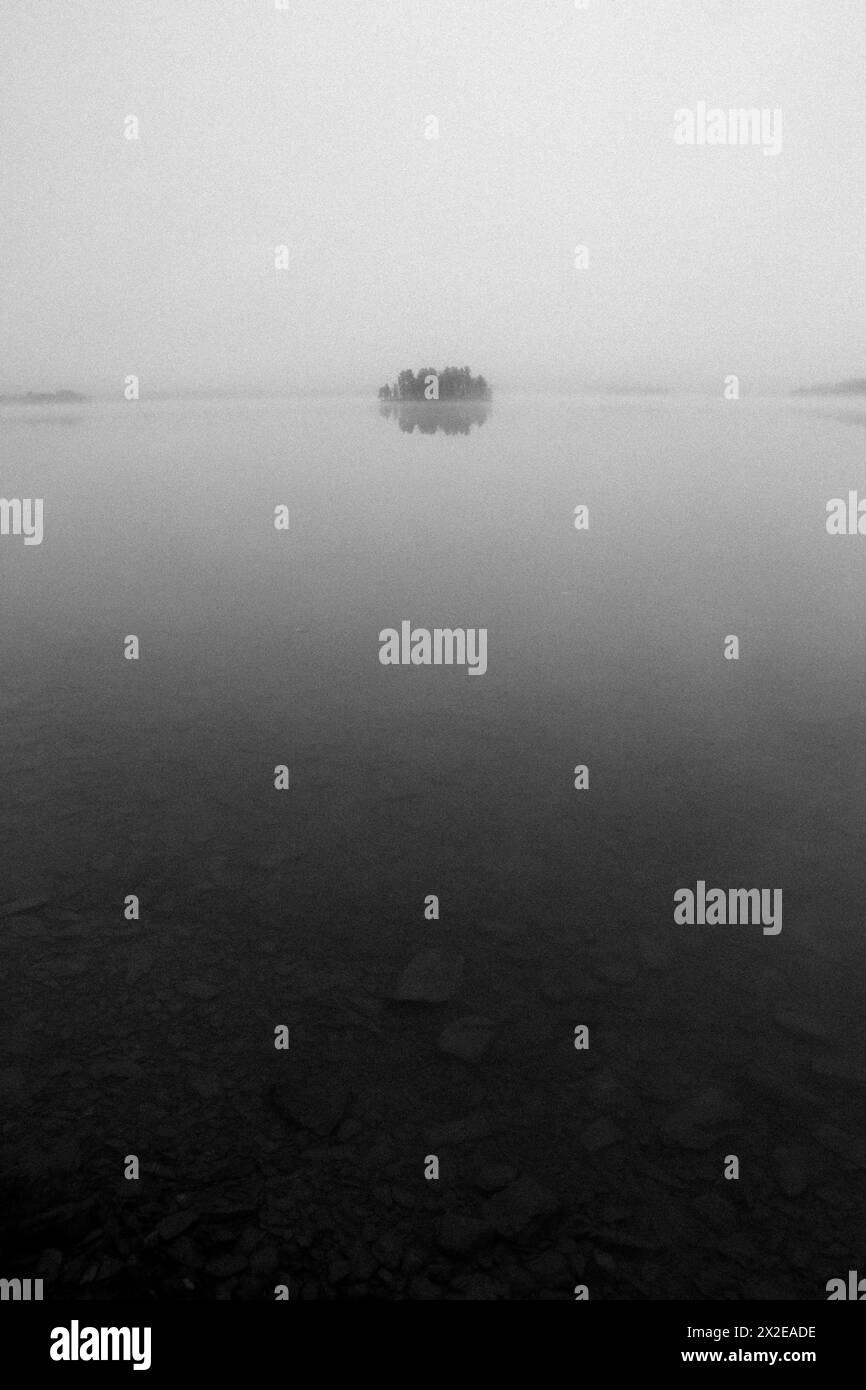 vista minimalista in bianco e nero dell'isola nel lago in nebbia e nebbia Foto Stock