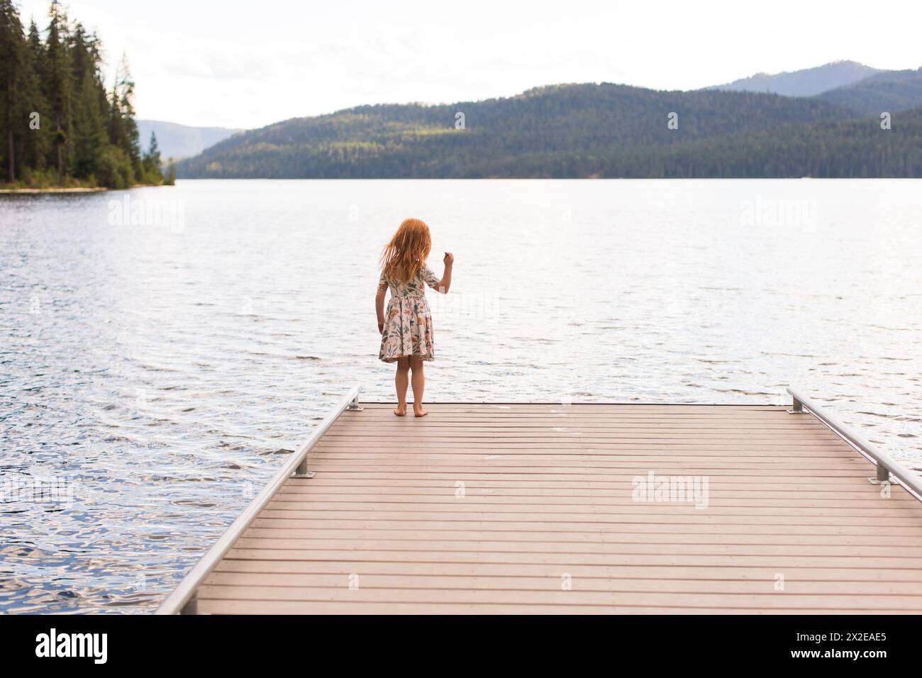 Redhead girl in piedi su un molo che getta roccia in un lago. Foto Stock