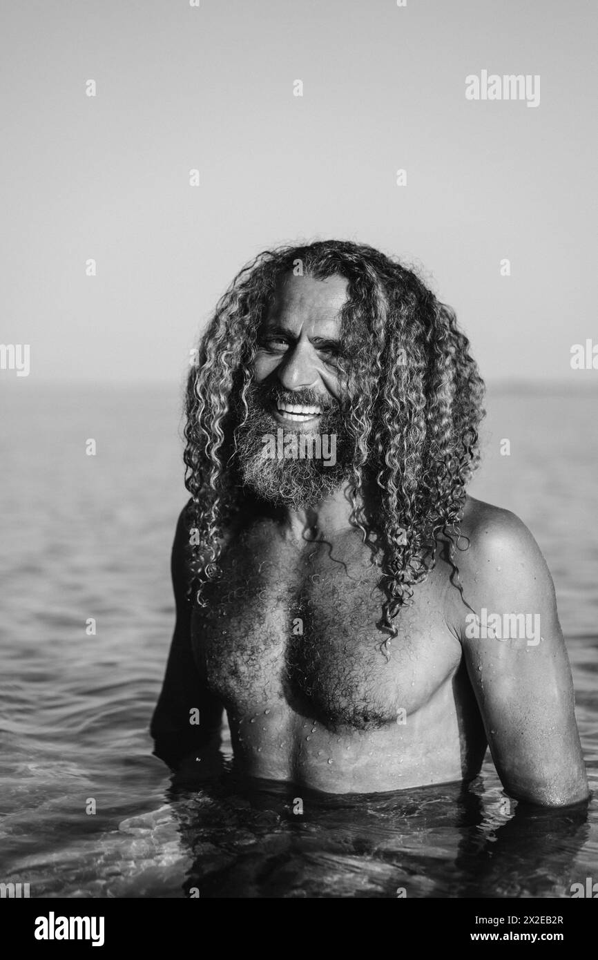 L'uomo con lunghi capelli ricci nuota nell'oceano. Foto Stock