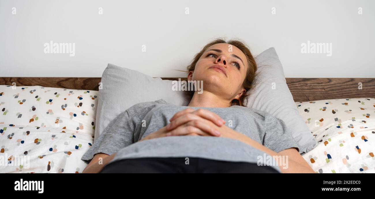 Stanca, affaticata, depressa, frustrata, sdraiata sul letto e con uno sguardo in alto senza parole. Malattia mentale e disperazione. Foto Stock