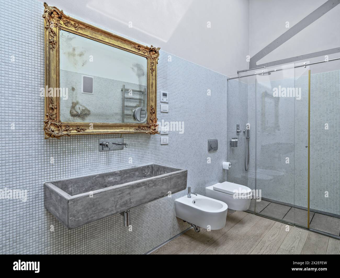 foto interne di un bagno moderno in primo piano, lavabo a parete in pietra con una cornice dorata sullo sfondo e box doccia in vetro Foto Stock