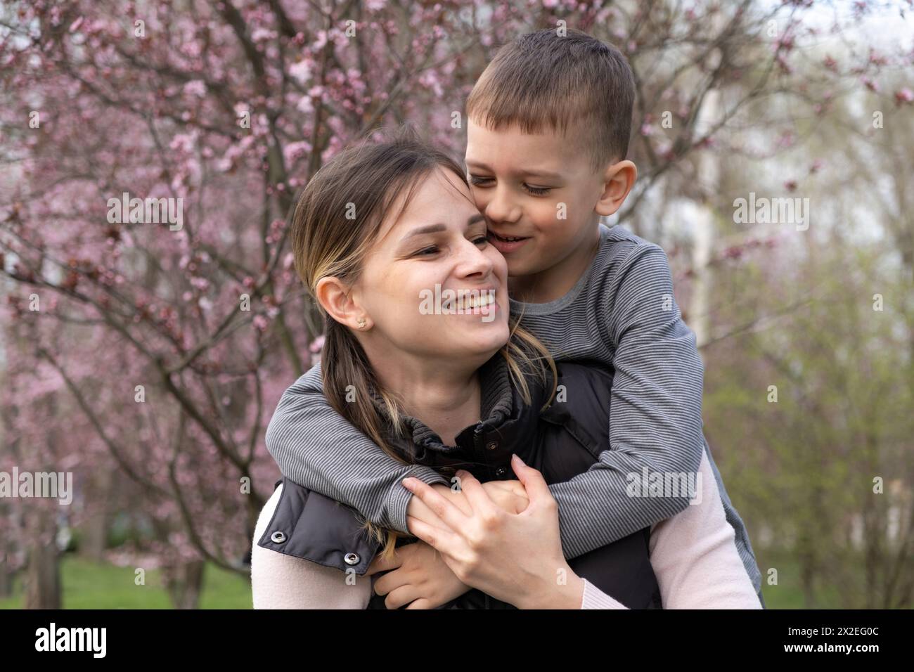 Mamma e figlio felici che si abbracciano tra i fiori di ciliegio in primavera. Foto Stock