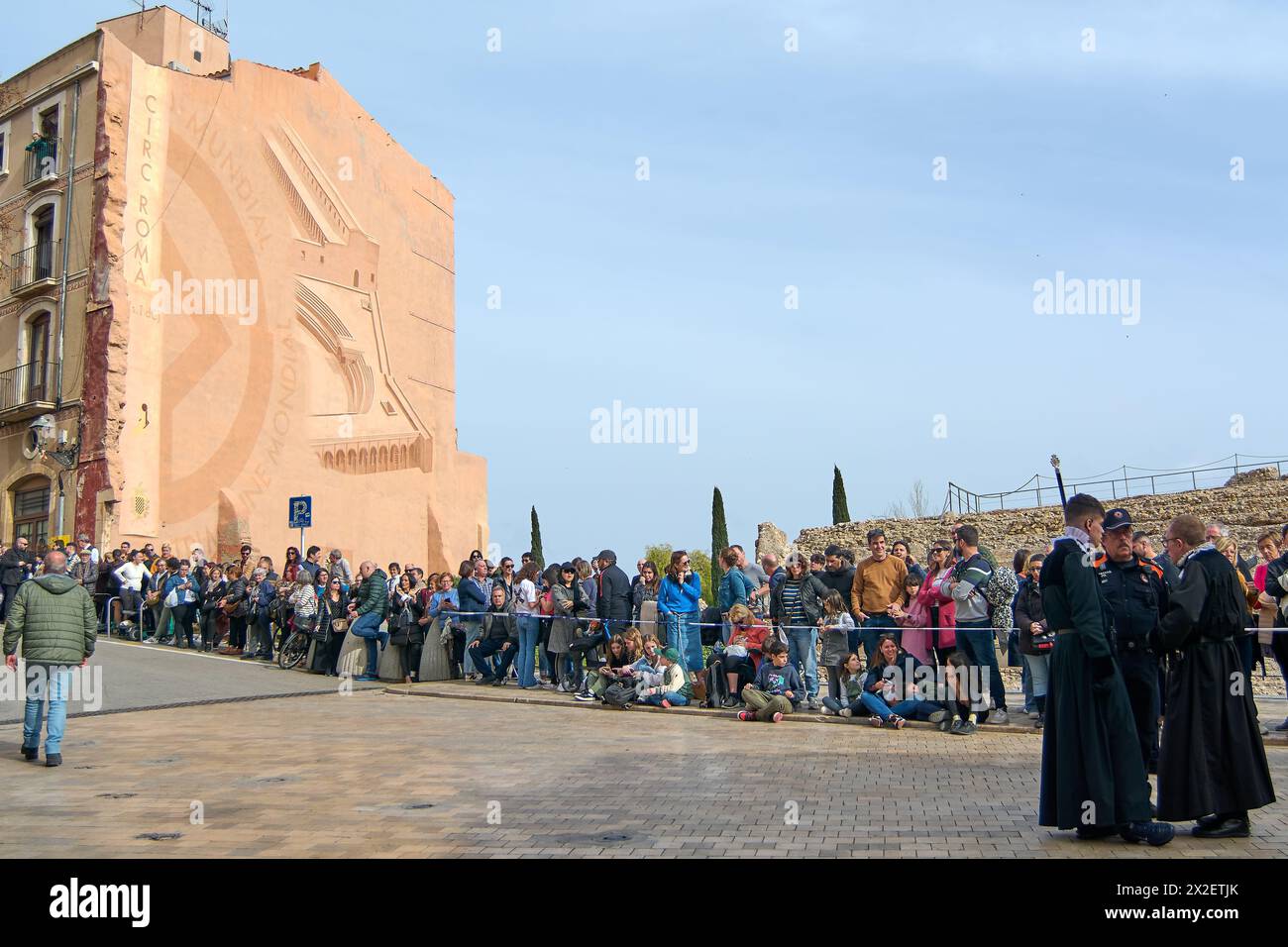 Tarragona, Spagna - 22 aprile 2024: Una folla si riunisce per assistere a una processione della settimana Santa a Tarragona con individui in abbigliamento tradizionale in mezzo a una sogliola Foto Stock